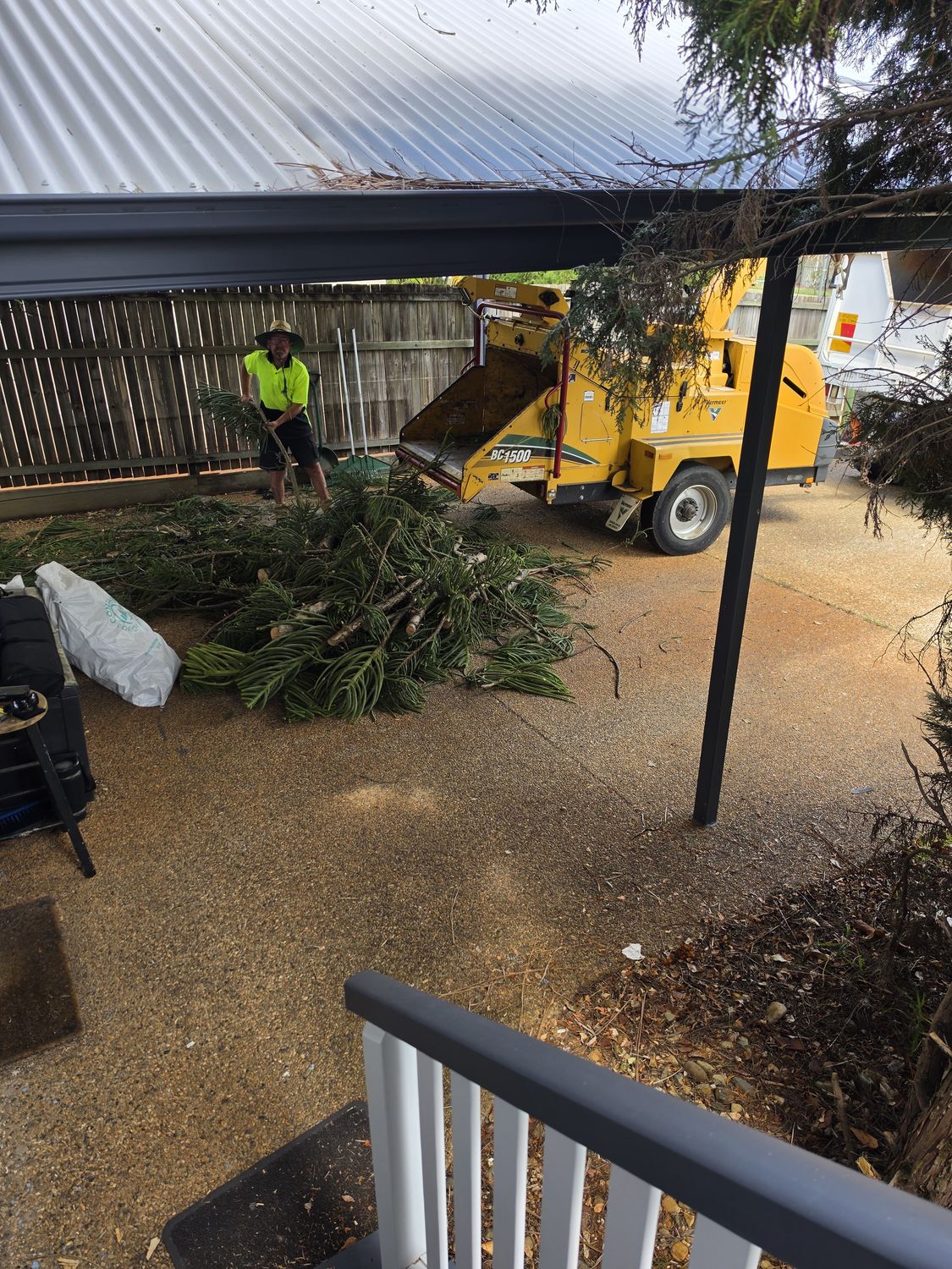 Crew member feeding branches into a yellow wood chipper under a carport
